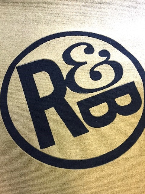 A tan carpet featuring a large black circle with the letters R&B in bold, stylized font inside the circle.